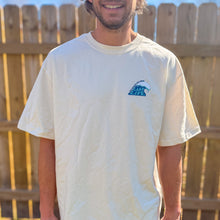 Load image into Gallery viewer, Person wearing a white t-shirt with a logo in front of a wooden fence