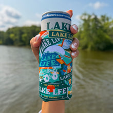 Load image into Gallery viewer, A hand holding a beverage can with a colorful illustrated sleeve that reads "LAKE LIFE" and "The Official Lake Life Day Drink," set against a blurred lake and trees background.