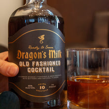 Load image into Gallery viewer, Bottle of Dragon's Milk Old Fashioned Cocktail with a glass of the cocktail on a wooden surface.