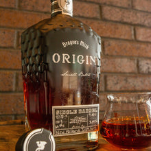 Load image into Gallery viewer, Bottle of Dragon's Milk Origin whiskey with a glass on a wooden surface against a brick wall.