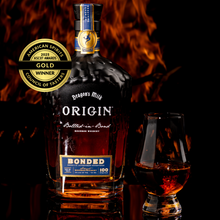Load image into Gallery viewer, A bottle of Origin Bonded with a glass of whiskey next to it and fire in the background.