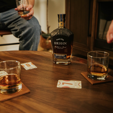 Load image into Gallery viewer, Two glasses of whiskey and a bottle labeled 'Origin' on a wooden table with playing cards.