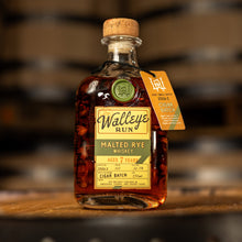 Load image into Gallery viewer, Walleye's Run Whiskey Cigar Batch bottle on a wooden barrel with blurred barrels in the background