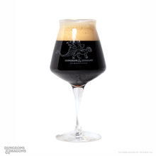 Load image into Gallery viewer, A clear stemmed beer glass with a dragon illustration and the text 'Dungeons & Dragons' on the front, filled with a very dark beer and topped with a thick golden foam head, photographed on a white background.