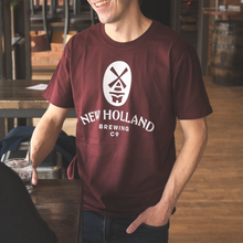 Load image into Gallery viewer, A person wearing a burgundy New Holland Brewing Co. classic t-shirt with a logo on the front.