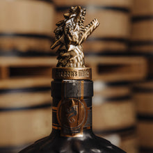 Load image into Gallery viewer, Dragon's Milk dragon pour spout with a decorative figure on top of a bottle, set against stacked barrels.
