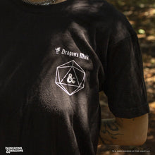 Load image into Gallery viewer, Person wearing a black t-shirt with a logo and text, standing in a forest.
