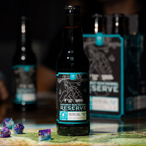 The is a photo of a bottle of Dragon's Milk x D&D Coconut Barrel Reserve with some dice in front of them.