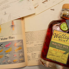 Load image into Gallery viewer, Bottle of Walleye Run Malted Rye Whiskey on a surface with papers and a book about water flies.

