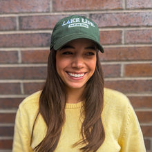 Load image into Gallery viewer, Woman wearing a green 'Lake Life Day Drinks' cap and yellow sweater in front of a brick wall.
