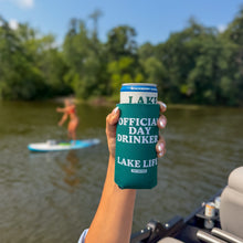 Load image into Gallery viewer, A hand holds a teal can cooler with white text reading 'OFFICIAL DAY DRINKER LAKE LIFE' in front of a blurred lake scene with a paddleboarder in the background.
