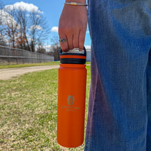 Load image into Gallery viewer, Person holding an orange water bottle with a blue sleeve outdoors.
