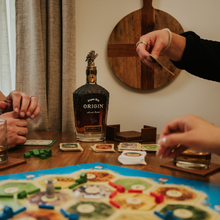 Load image into Gallery viewer, Two people playing a board game with a bottle of Origin Small Batch Bourbon Whiskey on a table.
