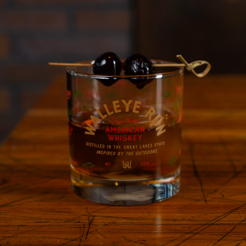 Glass of Walleye Run American Whiskey with cherries on a wooden surface