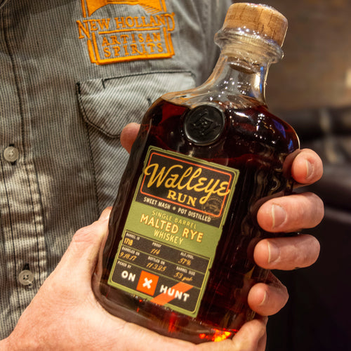 Hand holding a bottle of Walleye Run whiskey with a person wearing a shirt in the background.